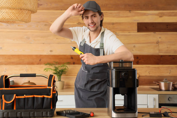 Trabalhador masculino com chave de fenda reparando máquina de café à mesa na cozinha - Foto, Imagem