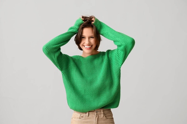 Счастливая молодая женщина в стильном зеленом свитере на сером фоне - Фото, изображение