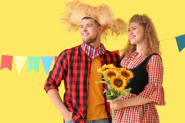 Glückliches junges Paar mit Fahnen und Sonnenblumen auf gelbem Hintergrund. Festa Junina - Foto, Bild