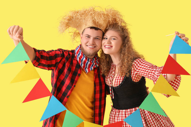 Glückliches junges Paar mit bunten Fahnen auf gelbem Hintergrund. Festa Junina - Foto, Bild