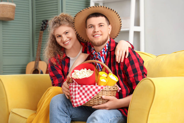 Šťastný mladý pár s popcornem sedící doma na gauči. Festa Junina oslava - Fotografie, Obrázek