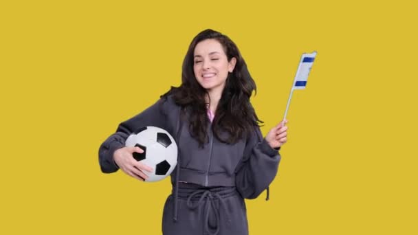 Onnellinen nuori naispuolinen fani poseeraa ja vilkuttaa Israelin lipun alla pitäen samalla jalkapalloa keltaisella eristetyllä - Materiaali, video