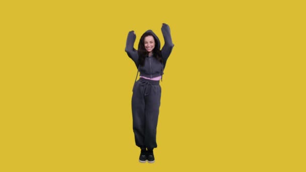 Smiling pretty lady enjoying while dancing, shaking hands up and jumping on yellow isolated. Full length. Lifestyle - Footage, Video