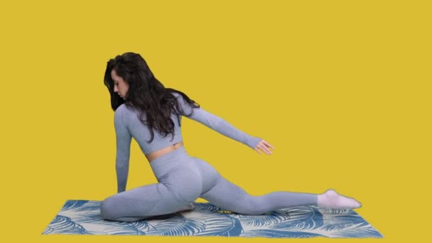 Joven mujer flexible haciendo yoga mientras estira las piernas, sentado en la esterilla de ejercicio sobre fondo aislado amarillo. Concepto de salud corporal - Metraje, vídeo