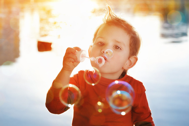 Little boy blowing soap bubbles at a lake - Φωτογραφία, εικόνα