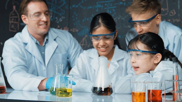 Девушка смотрит на стакан во время эксперимента на доске с теорией химии в классе STEM. преподаватель и группа школьников со смешанными расами занимаются научной деятельностью вместе. Назидание. - Фото, изображение