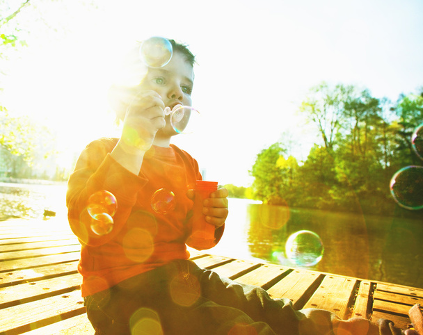 Little boy blowing soap bubbles at a lake - Foto, immagini