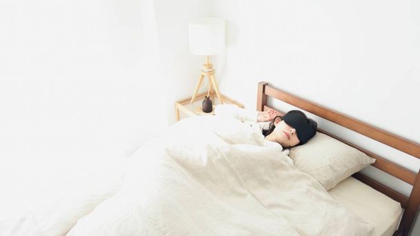 Una mujer durmiendo con una máscara en una habitación luminosa - Foto, Imagen