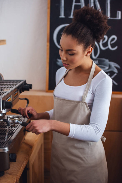 Belle barista afro-américaine dans le tablier prépare le café à l'aide d'une machine à café
 - Photo, image