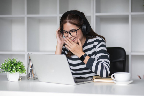 Όμορφη λογιστής φοράει ακουστικά για να συνομιλήσετε με συναδέλφους μέσω online πρόγραμμα κλήσης για την εργασία από την ημέρα στο σπίτι. - Φωτογραφία, εικόνα
