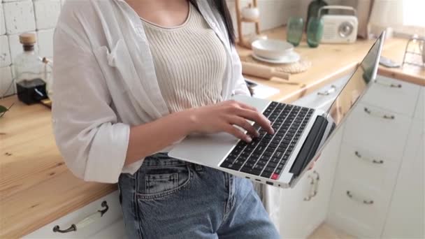 Close-up of young womans hands typing on laptop keyboard, resting on a kitchen countertop in a stylish, bright kitchen. Ideal for content on remote working, technology use, and modern kitchen setups. - Footage, Video