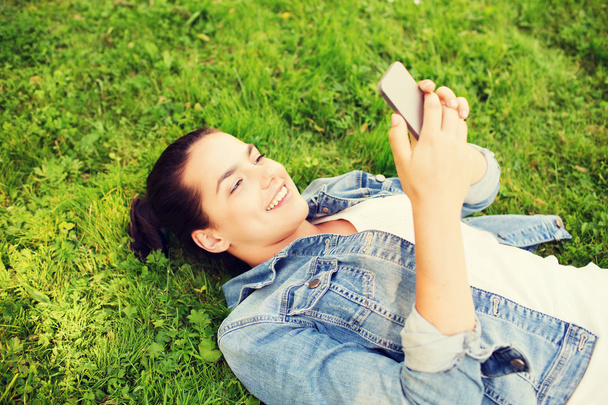 smiling young girl with smartphone lying on grass - Fotoğraf, Görsel