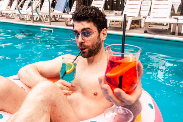 Mutlu sakallı adam, bir kokteyl içerken iki kokteyl tutuyor, açık havuzda dinleniyor. Yaz zamanı, tatiller, yaşam tarzı konsepti - Fotoğraf, Görsel