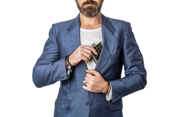 Man taking a flask out of his suit pocket. Male with beard put whiskey flask in pocket. Man drink alcohol. Flat metal bottle for alcohol. Bearded hipster in suit hold metal flask for alcohol. - Photo, Image