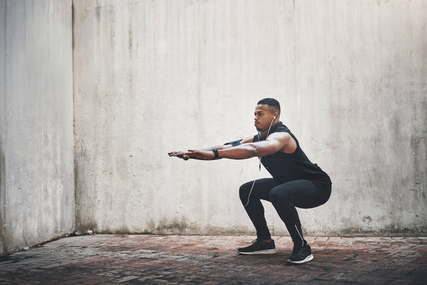 Mężczyzna, fitness i squatting ze słuchawkami w mieście dla silnych mięśni, równowagi lub ćwiczeń dla wellness. Mężczyzna osoba, muzyka i trening dla nóg ze słuchaniem, zdrowie lub audio streaming w Nowym Jorku. - Zdjęcie, obraz