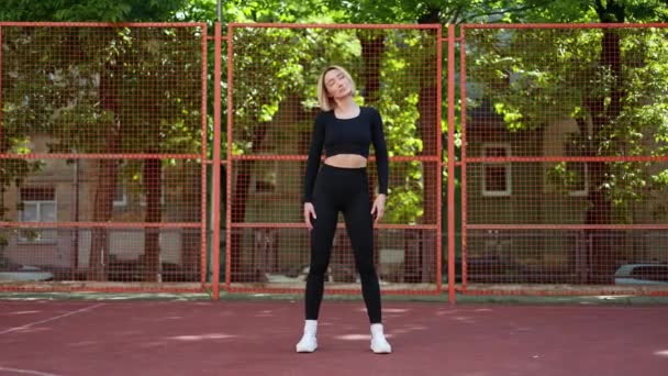 Жінка в спортивному одязі тягнеться на баскетбольному майданчику. Спортивна дівчина готується до тренування - Кадри, відео