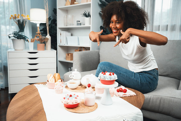 Belle jeune blogueuse africaine présentant un morceau de cupcake en concept montrant une cuisine spéciale en couleur pastel. Création de contenu de médias sociaux avec plat préféré de boulangerie de bonbons. Tastemaker. - Photo, image