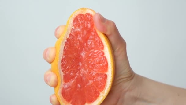 Рука стискає грейпфрутовий сік з половини грейпфрута на білому фоні - Кадри, відео