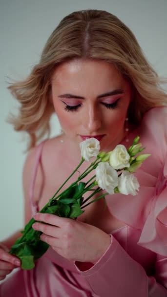 Rózsaszín ruhás szőke, gyengéden fehér virágcsokrot tart.. - Felvétel, videó
