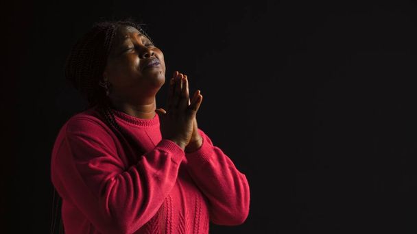 Mujer negra elegante mirando hacia arriba con las palmas extendidas en gesto de reverencia y adoración. Retrato de vista lateral de una dama afroamericana comprometida en una reflexión piadosa en un fondo aislado. - Foto, imagen