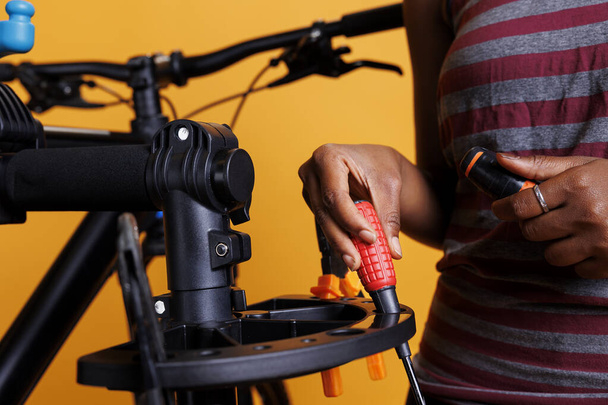 Close-up van Afro-Amerikaanse vrouwelijke hand het organiseren van de nodige fiets service tools. Fotofocus op schroevendraaier en andere gespecialiseerde uitrustingen die door een individu op de fietsenstandaard worden geplaatst. - Foto, afbeelding