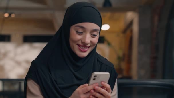 musulmana chica árabe islámica mujer en hijab feliz mujer de negocios empresaria gerente de oficina ejecutivo utilizando el teléfono móvil escribiendo SMS mensaje de texto en línea teléfono inteligente chateando sonriendo - Imágenes, Vídeo