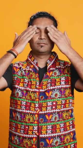 Dikey videocu adam geleneksel Hint kıyafetleri giyer, gözleri, kulakları ve ağzı kaplar, üç bilge maymunu taklit eder, görmez, duymaz ve el hareketi konsepti, stüdyo arka planı, - Video, Çekim