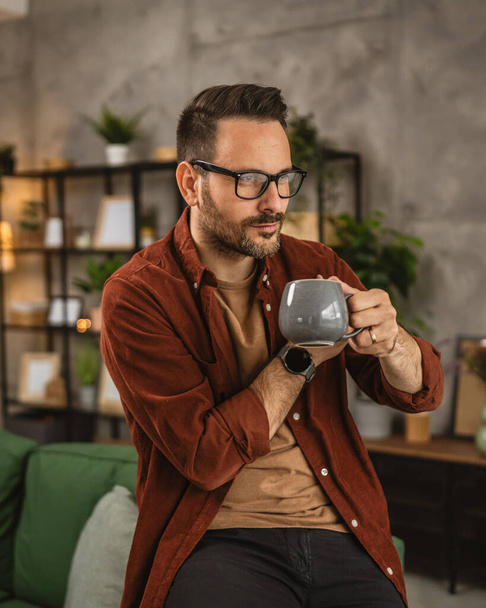 Adult caucasian man sit and hold coffee look out the window at home - Photo, Image