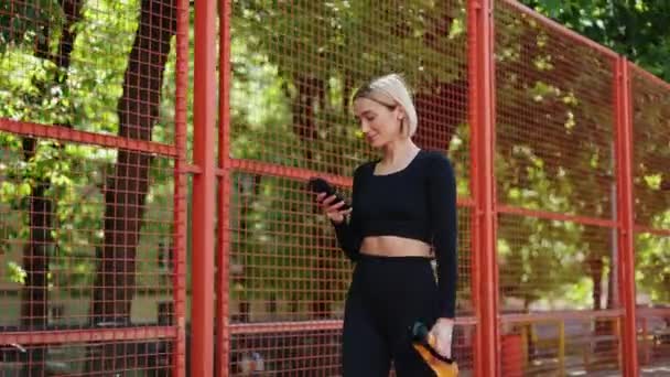 Happy fit nő ellenőrzi a telefonját, élvezi a pihenés pillanatát edzés után. - Felvétel, videó
