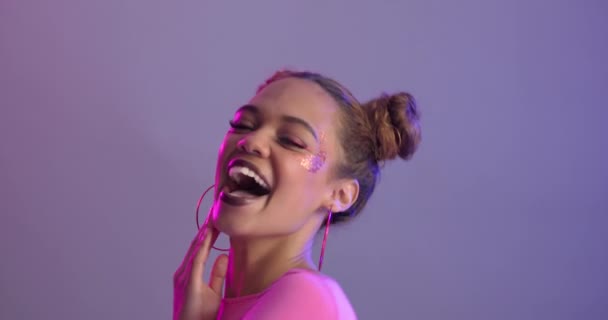 Woman, beauty and makeup with energy, crazy and goofy with earrings and glitter on purple background. Fun, playful and pout in portrait with funny face, space buns hairstyle and funky style in studio. - Footage, Video