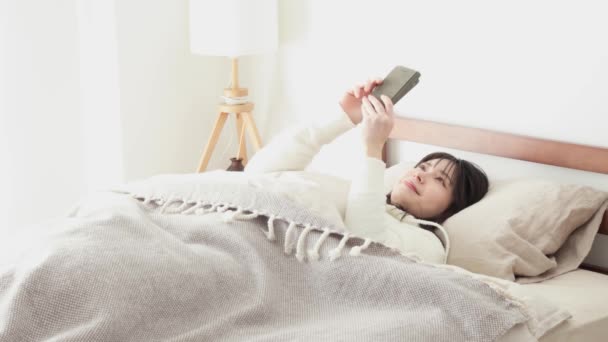 Femme asiatique regardant smartphone après le réveil - Séquence, vidéo