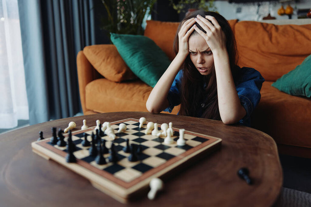 Donna che contempla la sua prossima mossa durante un'intensa partita a scacchi, seduta su un divano con una scacchiera - Foto, immagini