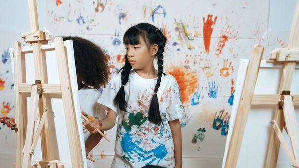 Playful student painted or draw canvas at stained wall with diverse friends in art lesson. Group of happy multicultural children working or create artwork at messy room. Creative activity. Erudition. - Photo, Image