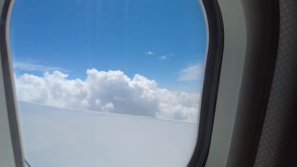 Blick aus dem Flugzeugfenster über weiße Wolken und blauen Himmel - Filmmaterial, Video