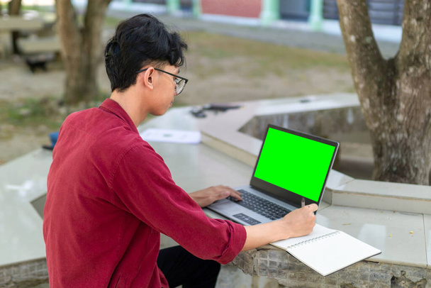 Asijský vysokoškolák studující na notebooku v kampusu venkovní park. Muž, který píše do sešitu a pracuje na laptopu. Koncepce vzdělávání - Fotografie, Obrázek