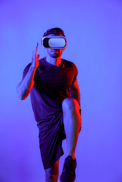 ネオンライトでVRゴーグルを着用しながらジョギングする白人スマートな男. バーチャルリアリティヘッドセットを使用している間,カジュアルな布のランニングやエクササイズで幸せな人. イノベーション技術コンセプト。 デバイス. - 写真・画像