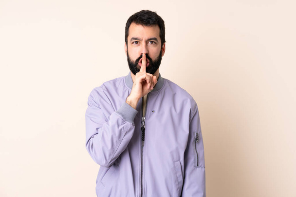 Biały mężczyzna z brodą w kurtce na odosobnionym tle, pokazujący znak milczenia, wkładający palec do ust. - Zdjęcie, obraz
