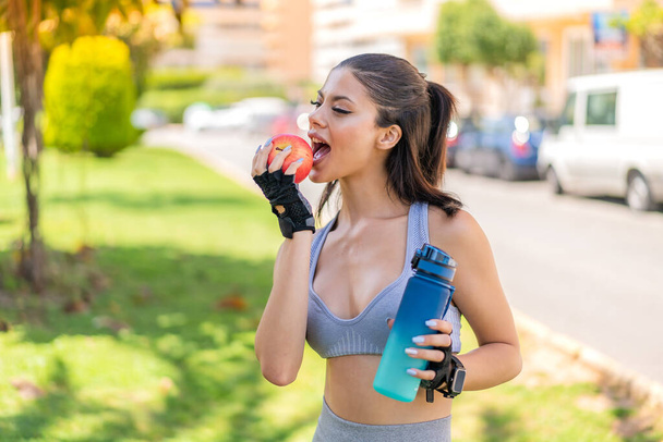 Jonge mooie sport vrouw buiten met een appel en een fles water - Foto, afbeelding