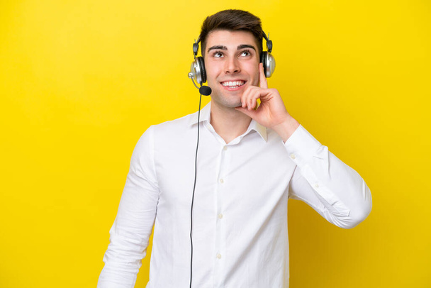 Telemarketer καυκάσιος άνθρωπος που εργάζονται με ένα ακουστικό που απομονώνονται σε κίτρινο φόντο σκέφτεται μια ιδέα, ενώ κοιτάζοντας προς τα πάνω - Φωτογραφία, εικόνα