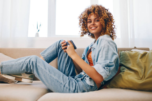 Szczęśliwa kobieta trzyma smartfona i uśmiecha się relaksując się na wygodnej sofie w domu - Zdjęcie, obraz