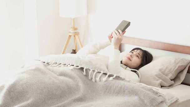 Asian woman looking at smartphone after waking up - Photo, Image