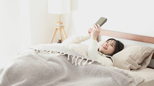 Азиатка смотрит на смартфон после пробуждения - Фото, изображение