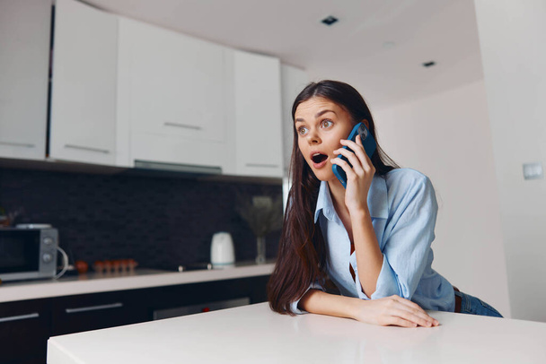 Mutfak masasında cep telefonu kullanan bir kadın, modern ev ortamında gündelik konuşma, teknoloji ve iletişim kavramı - Fotoğraf, Görsel