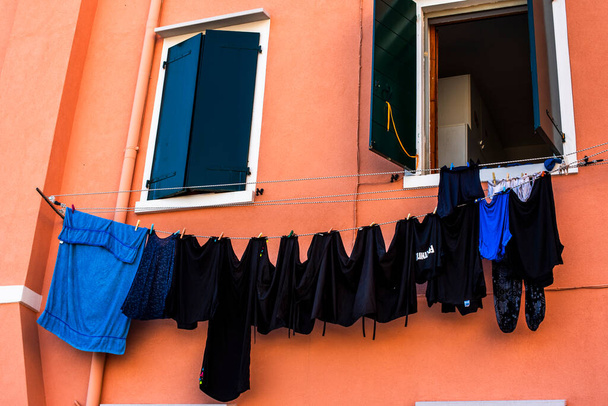 Wäsche hängt in der Herbstsonne in der Stadt Pellestrina an der Lagune von Venedig schwarze T-Shirts hängen an einer ziegelfarbenen Wand - Foto, Bild