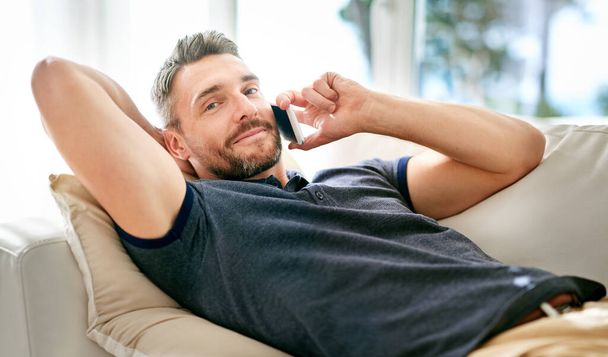 Portrait, Mann und Couch auf Abruf mit Smartphone genießen freien Tag von der Arbeit, reden und Netzwerk auf digitale Technologie. Glückliche, männliche Person und Entspannung zu Hause in Lounge auf dem Handy zu kommunizieren. - Foto, Bild