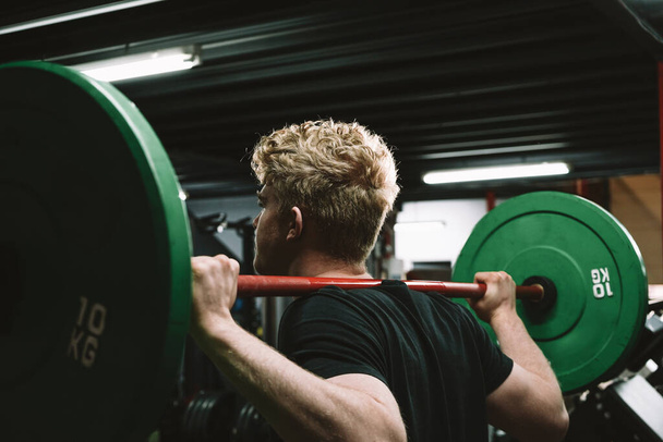 Vista trasera de un atleta masculino fuerte haciendo ejercicio con una barra en el gimnasio crossfit - Foto, imagen