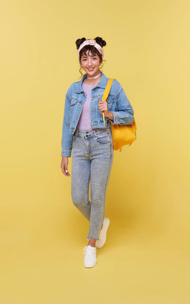 Портрет счастливой улыбающейся молодой азиатской студентки с рюкзаком, готовой к школе изолированы на желтом фоне. - Фото, изображение