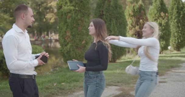 Twee studenten gaan in gesprek over de universiteit wanneer hun vrouwelijke collega zich aansluit, begroeten hen met een positieve houding, het toevoegen van een vrolijke sfeer aan hun gesprek. - Video