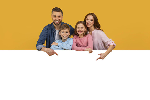 Een gelukkig gezin, bestaande uit een vader, moeder, zoon en dochter, poseren vrolijk voor een portret. Ze zijn casual gekleed en comfortabel leunend op een wit oppervlak, mockup, kopieerruimte - Foto, afbeelding