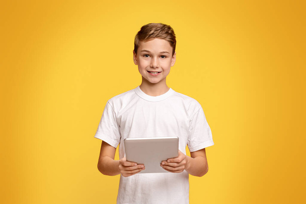 Tiener jongen met behulp van digitale Tablet, online browsen of spelen game app op oranje studio achtergrond - Foto, afbeelding
